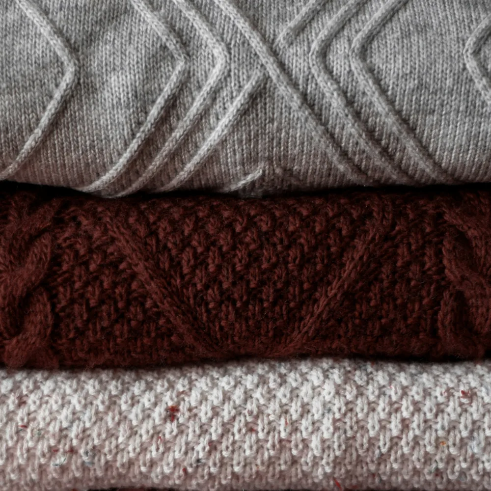 Stack of folded knitted jumpers in grey, maroon and oatmeal